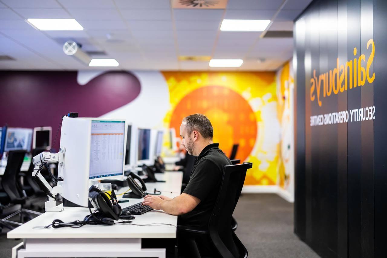 Mitie employee at a computer in the Security Operations Centre, with Sainsbury's branding on the walls
